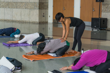 traci ishigo assists a yogi with a pose. Photo by Ben Furuta.